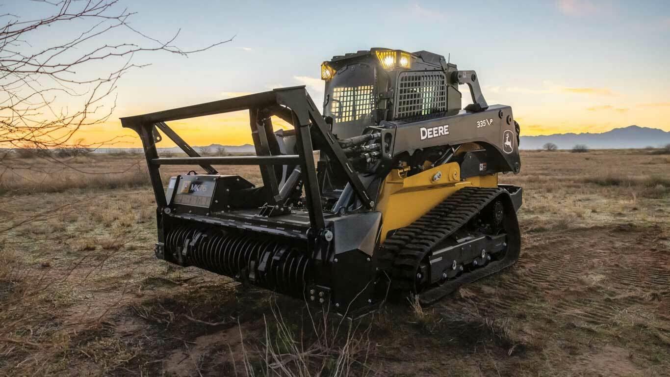 335 P-Tier Skid Steer with Tracks and MK76 Mulching Head attachment with mountains and sunset scene in the background